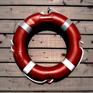 A red life ring hanging on the side of a wooden wall.