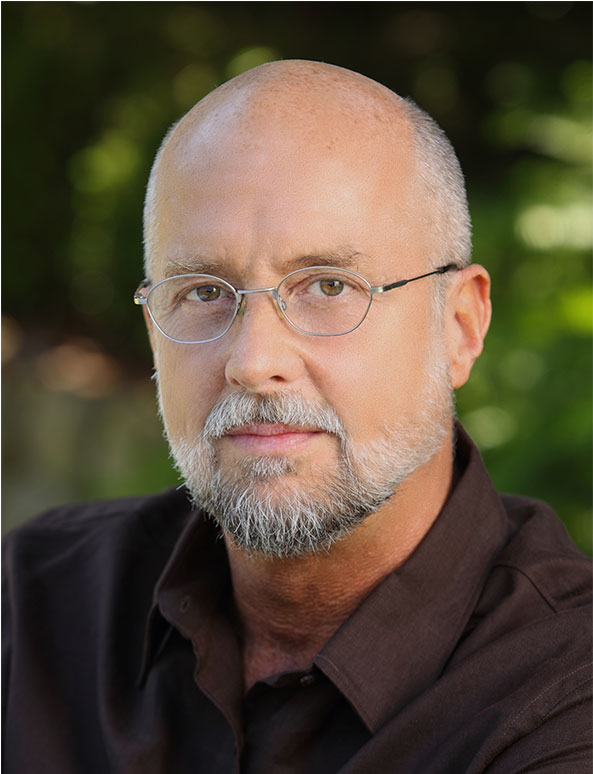 A man with glasses and a beard wearing a brown shirt.