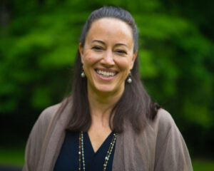 A woman smiling for the camera in front of trees.