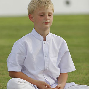 A young boy sitting in the grass meditating.